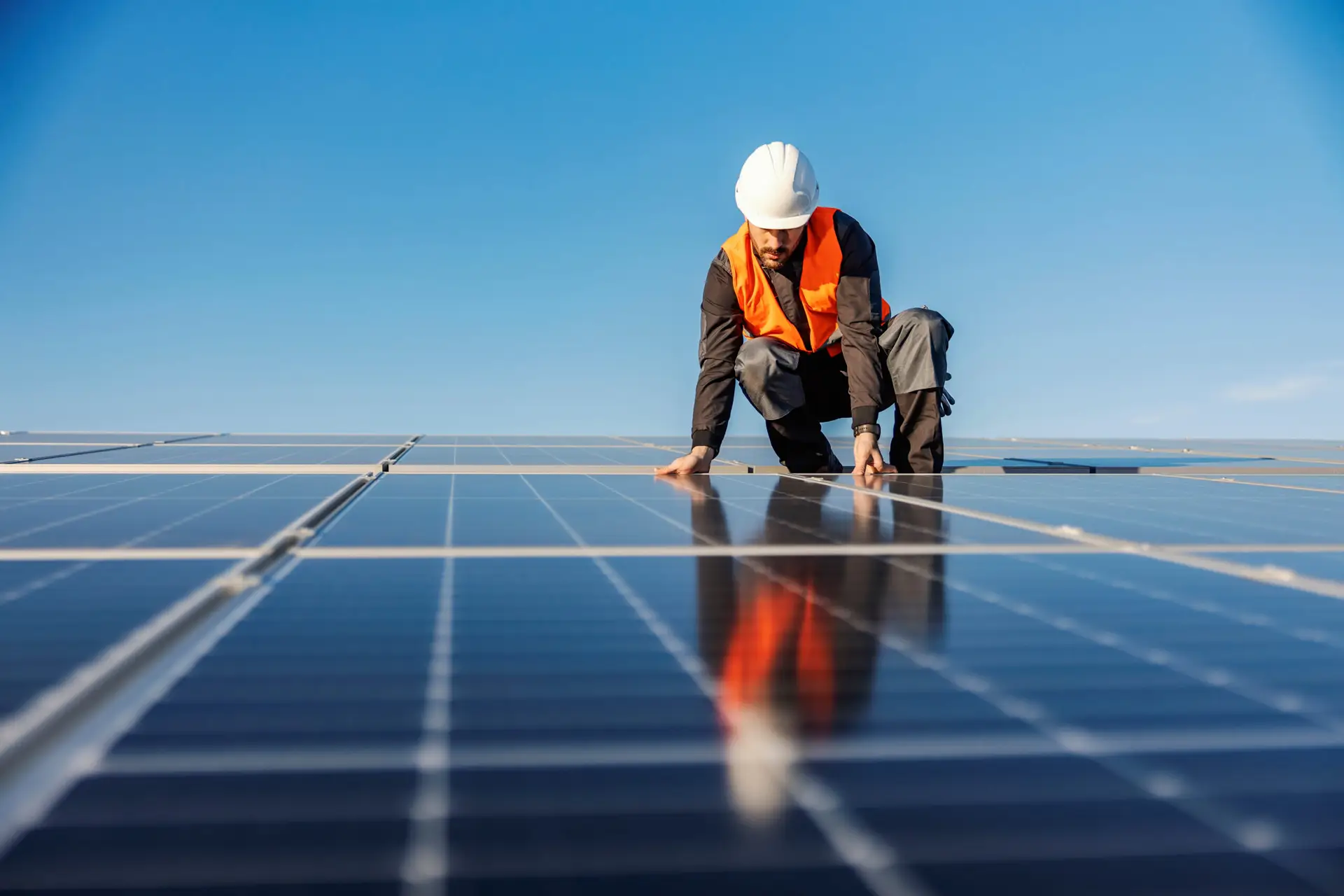 a man in a white helmet and orange vest on solar panels